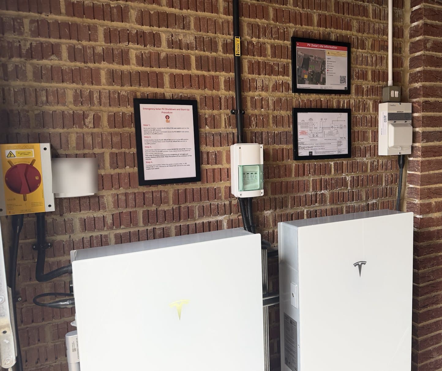 Twin Tesla Powerwall batteries installed in a garage with clear shutdown and site information notices